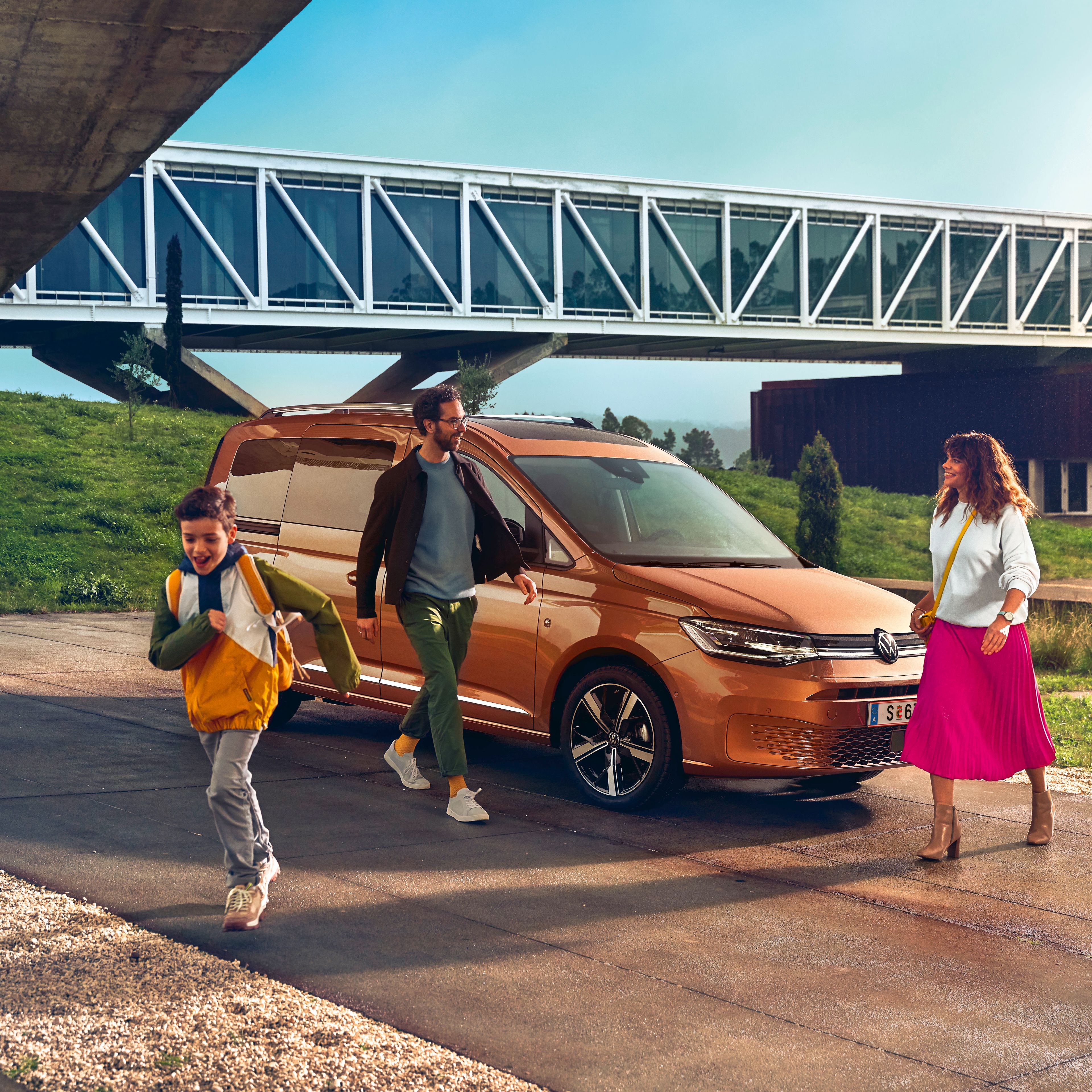 Ein VW Caddy 2020 parkt vor einer Brücke. Eine Familie geht gerade vom Auto weg.